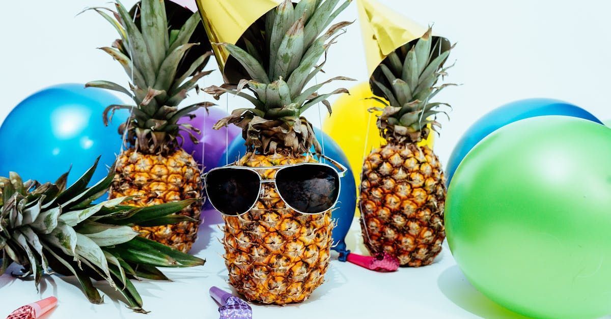 Pineapples with sunglasses, surrounded by balloons and party decorations.