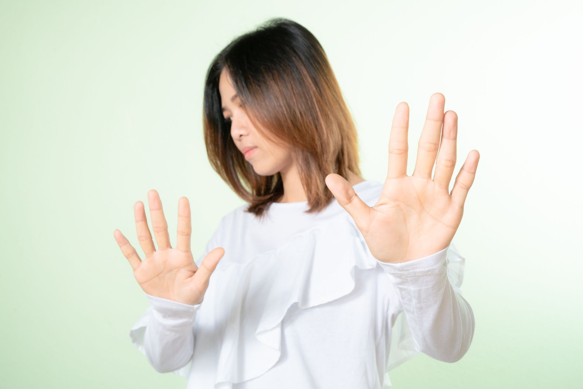 Woman with palms out, defensive gesture, white shirt, light green background.