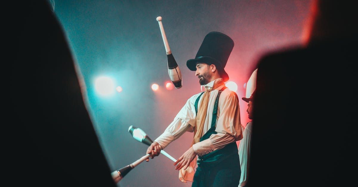Juggler in top hat throws clubs in stage spotlight.