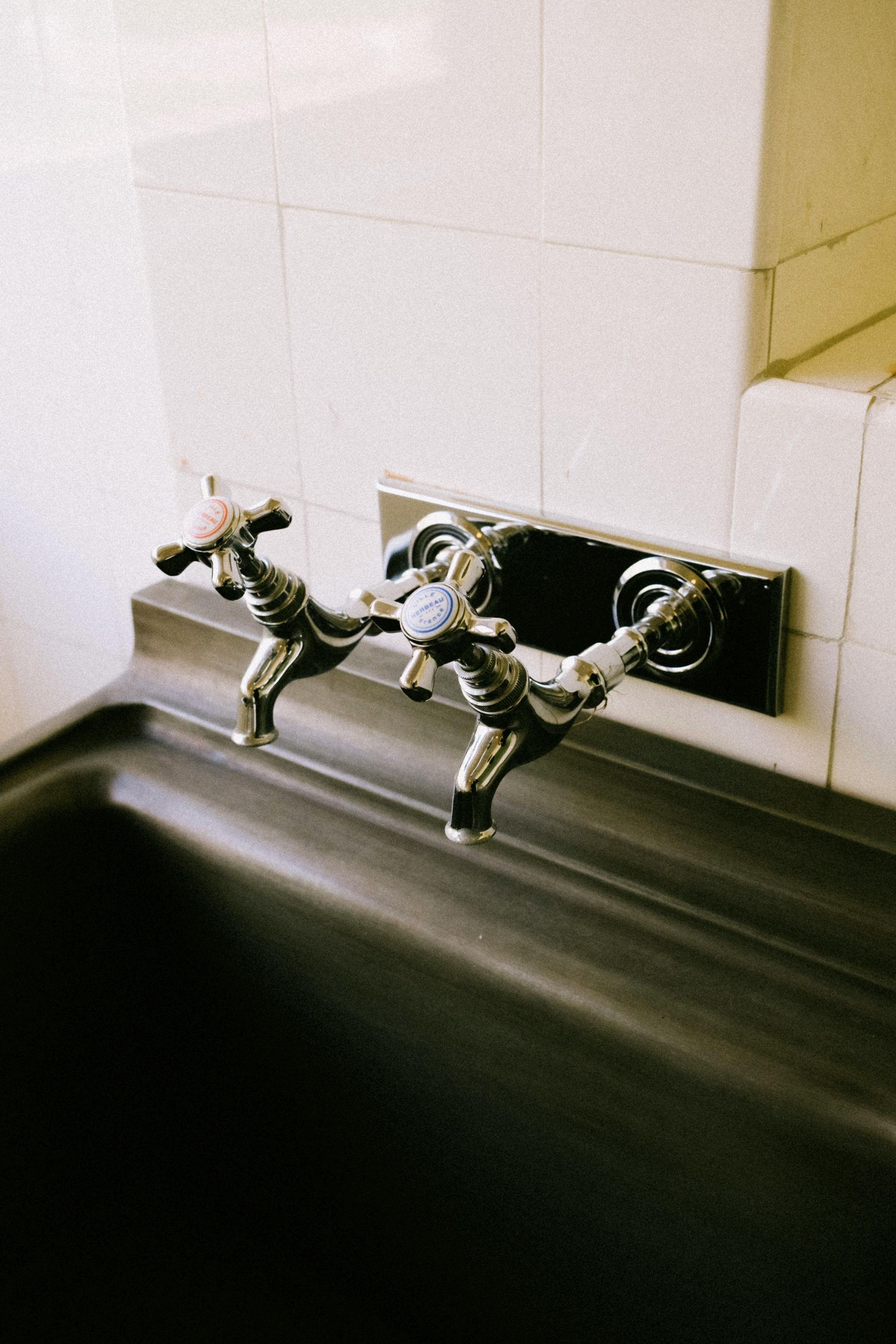 Two chrome faucet handles above a dark sink against a tiled wall.
