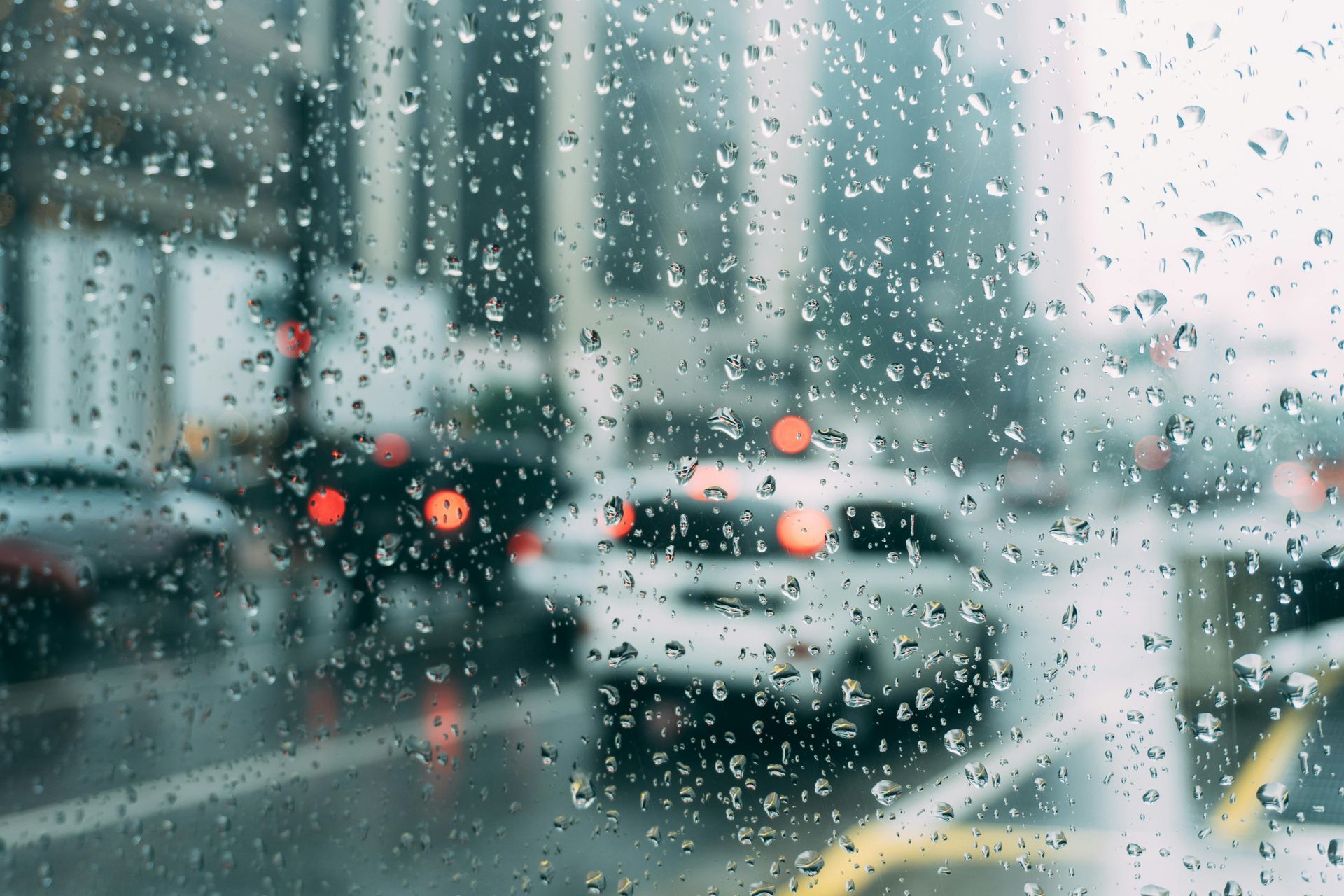 Raindrops on a window, blurred cityscape with cars and buildings in the background.