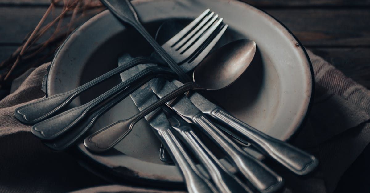 Silverware piled on a white plate with a dark cloth; rustic setting.