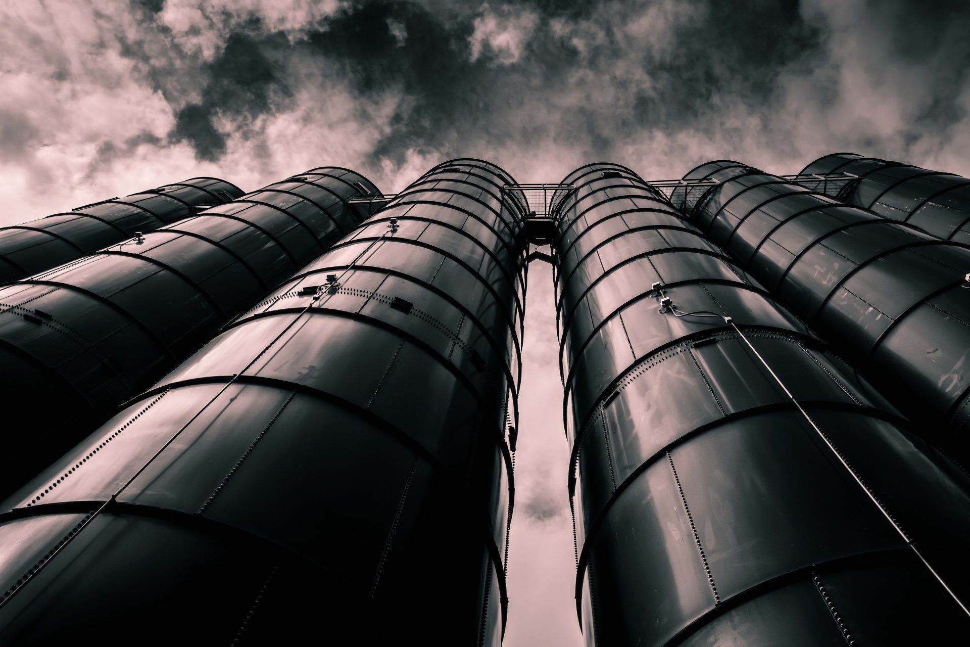 Steel storage tanks against a cloudy sky, seen from below.