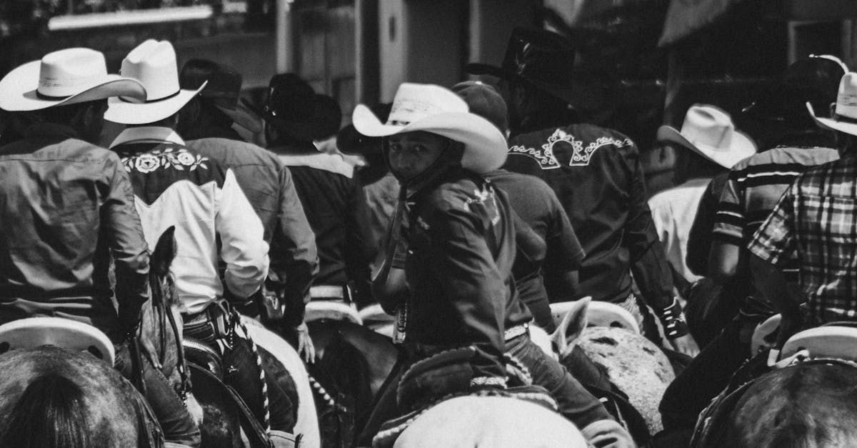 Cowboys on horseback, wearing hats, gathered at an event, some smiling. Black and white.