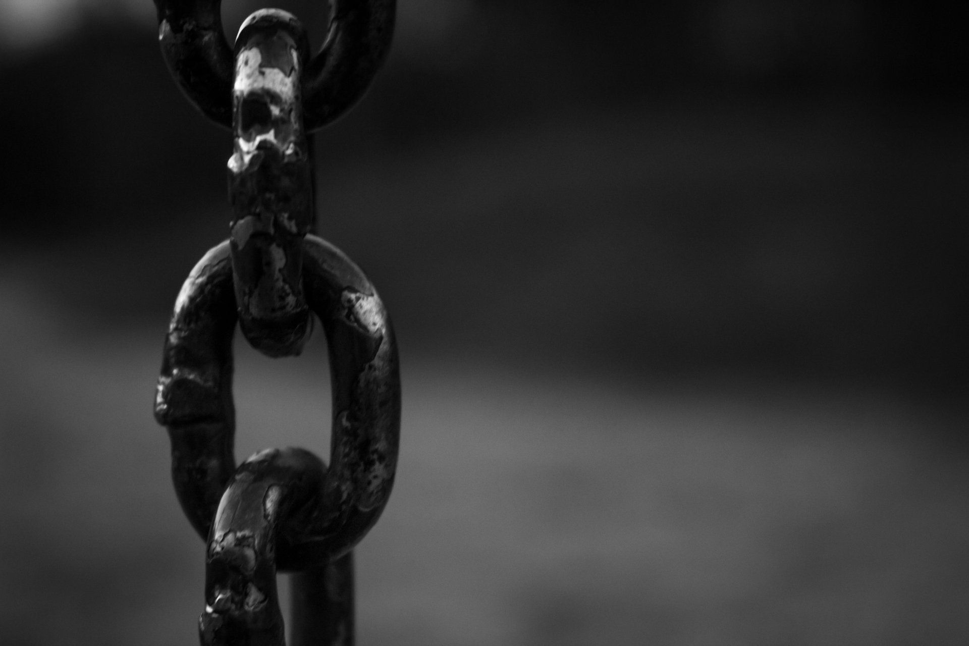 Close-up of a weathered, metal chain, hanging against a blurred background.