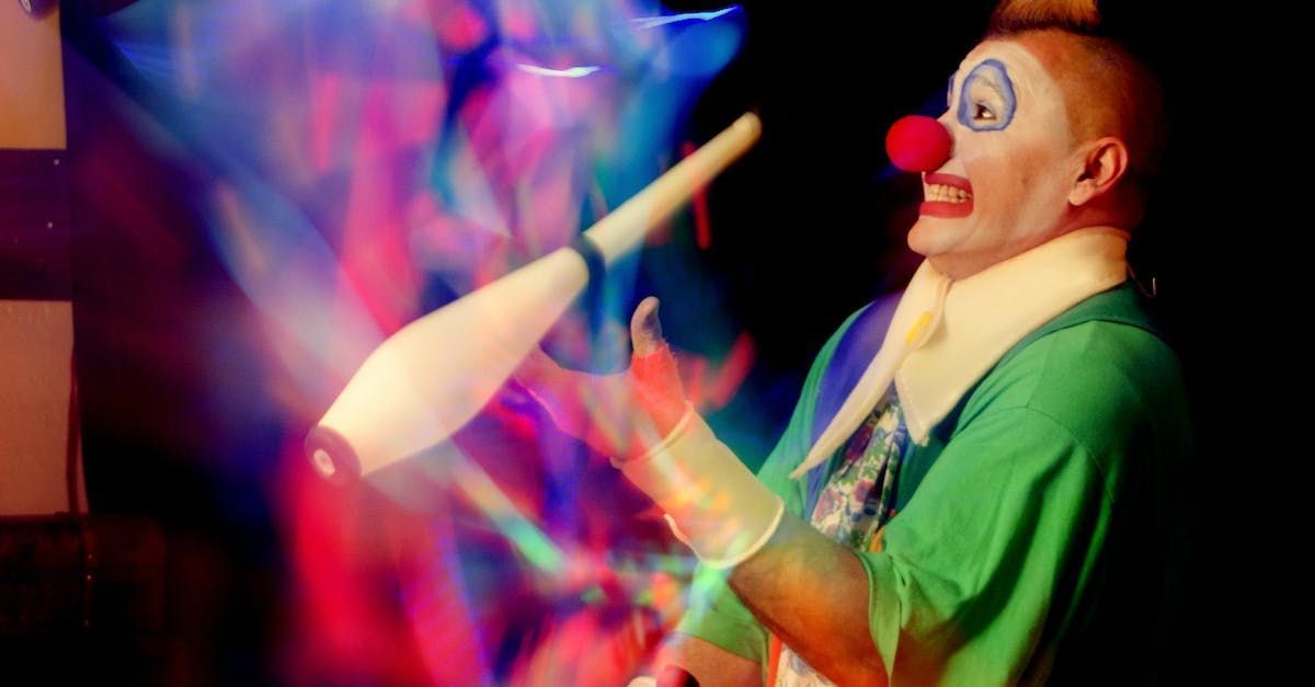 Clown juggling white clubs with blurred light streaks, smiling against a dark background.