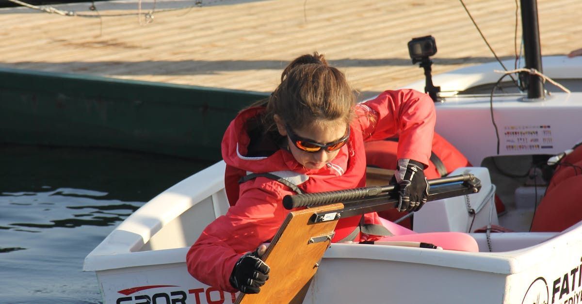 A person in a red jacket and sunglasses prepares a boat for rowing on water.