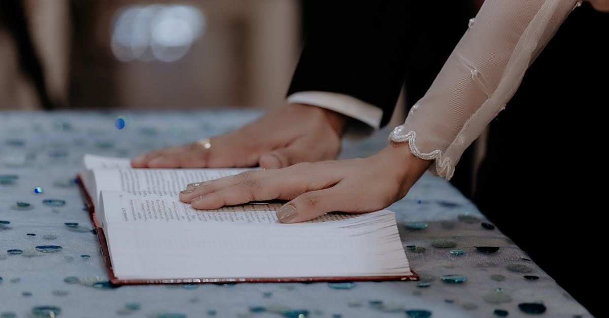 Hands of a couple on an open book, possibly during a wedding ceremony. Rings visible.