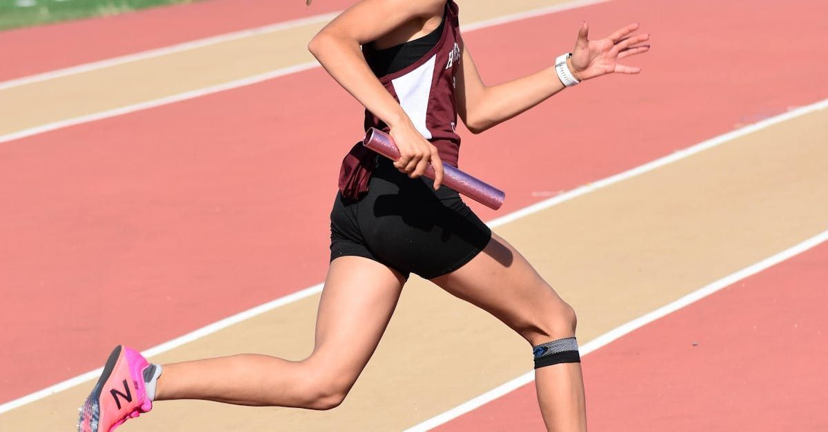 Runner on a track in a maroon and black uniform, holding a baton, in motion.