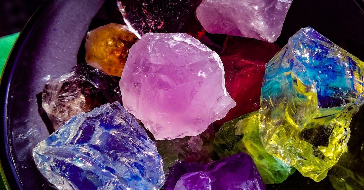 Close-up of a bowl filled with colorful, raw gemstones in shades of purple, blue, yellow, red, and orange.