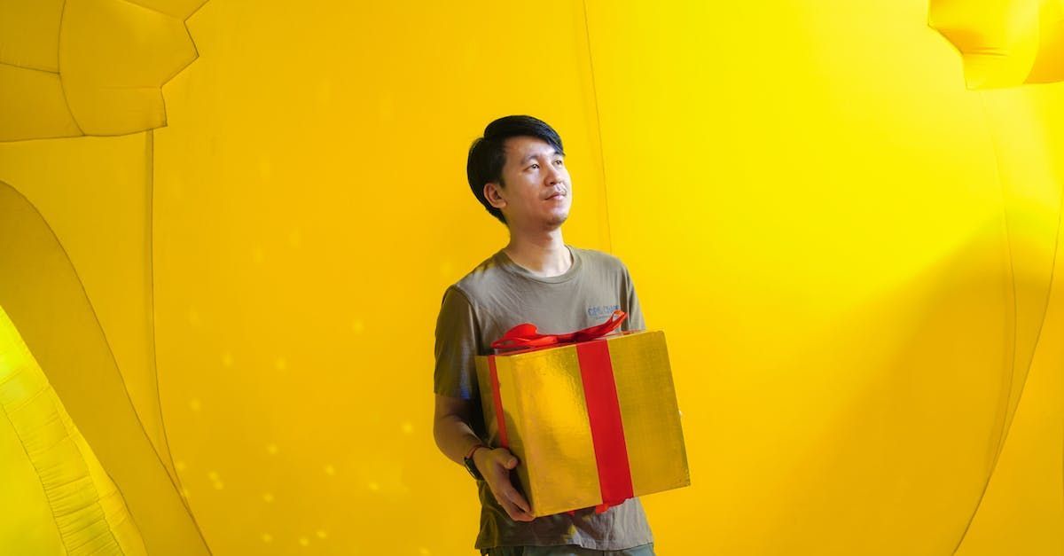 Man in gray shirt holding a gift against a yellow backdrop, looking upward.