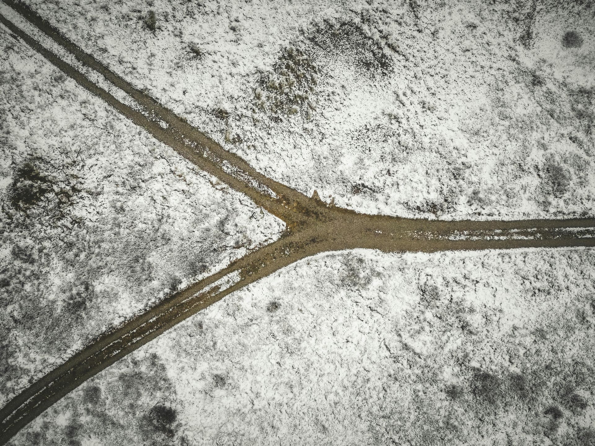 Overhead view of three dirt roads meeting in a snowy field.