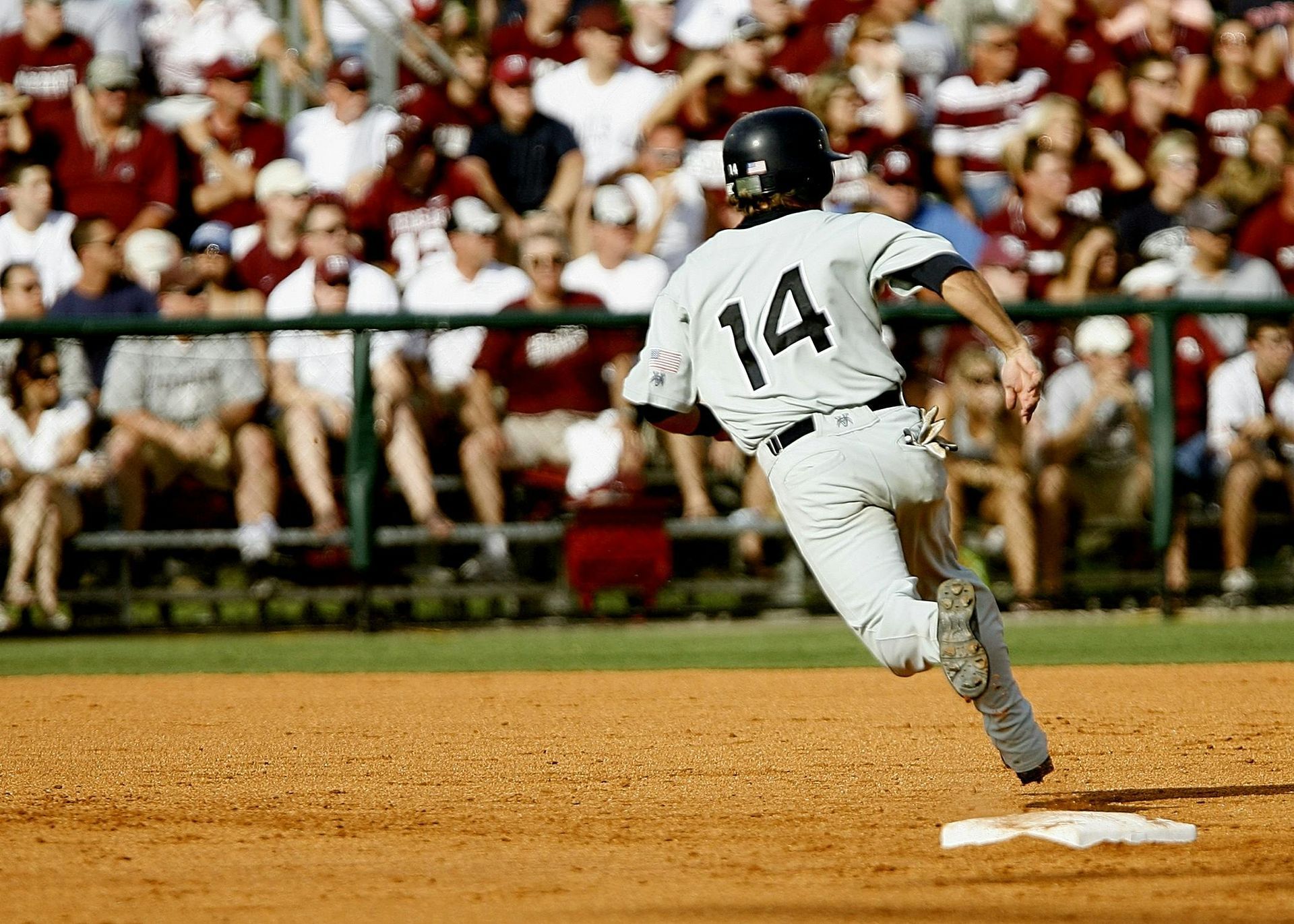 Baseball player wearing jersey number 14 runs toward a base on a baseball field, with a crowd in the background.
