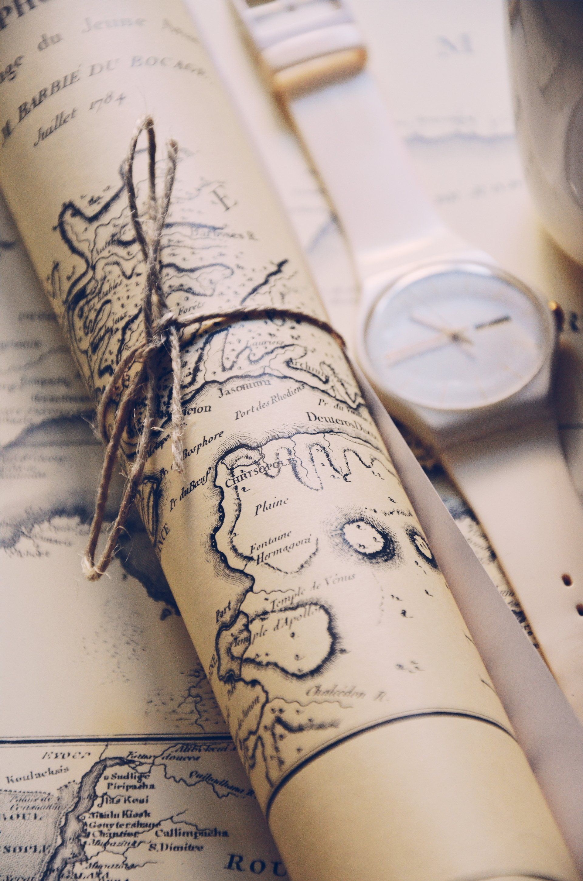 Rolled map tied with twine, next to a wristwatch and other maps, suggesting exploration.