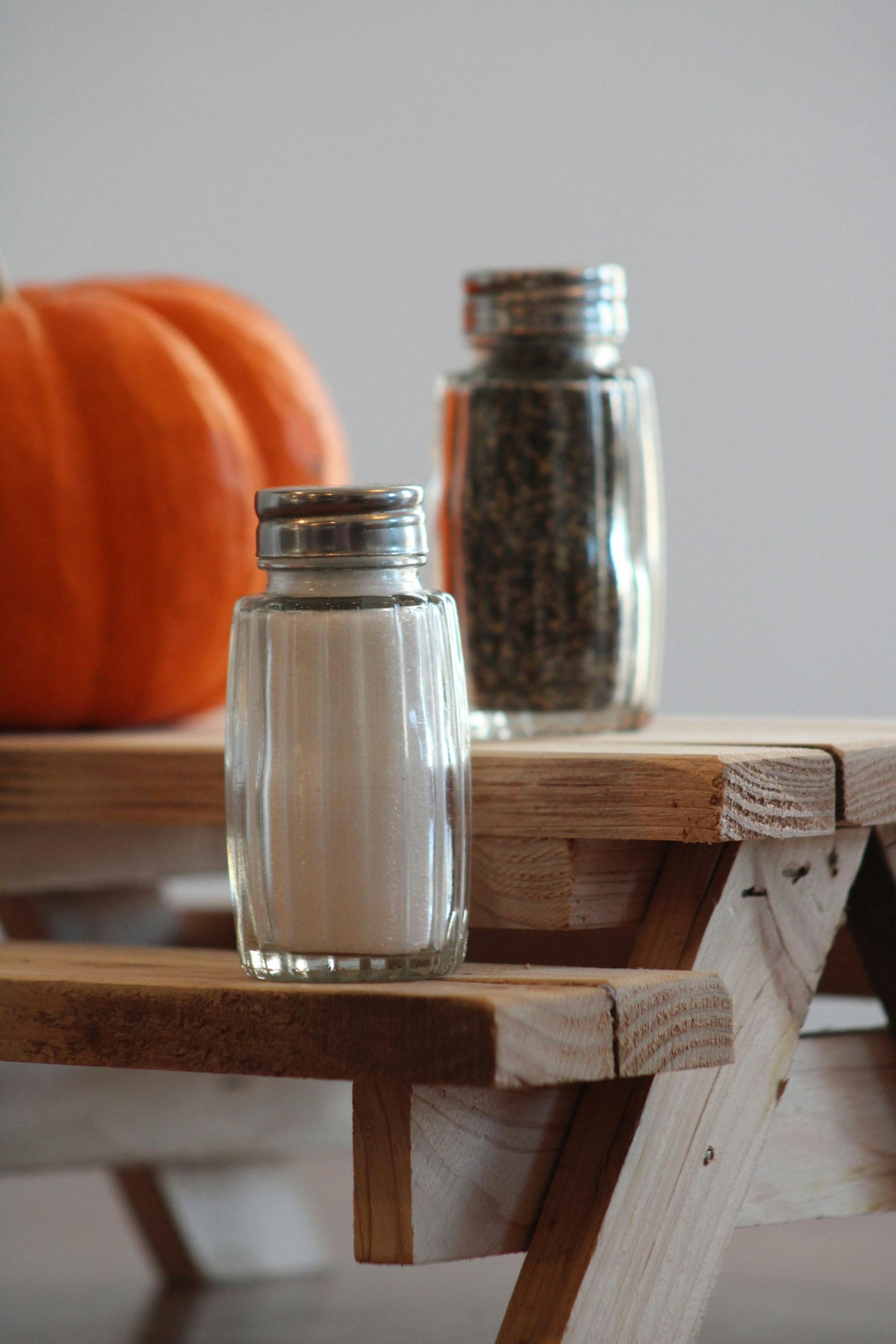 Salt and pepper shakers on miniature wooden picnic table with an orange pumpkin.