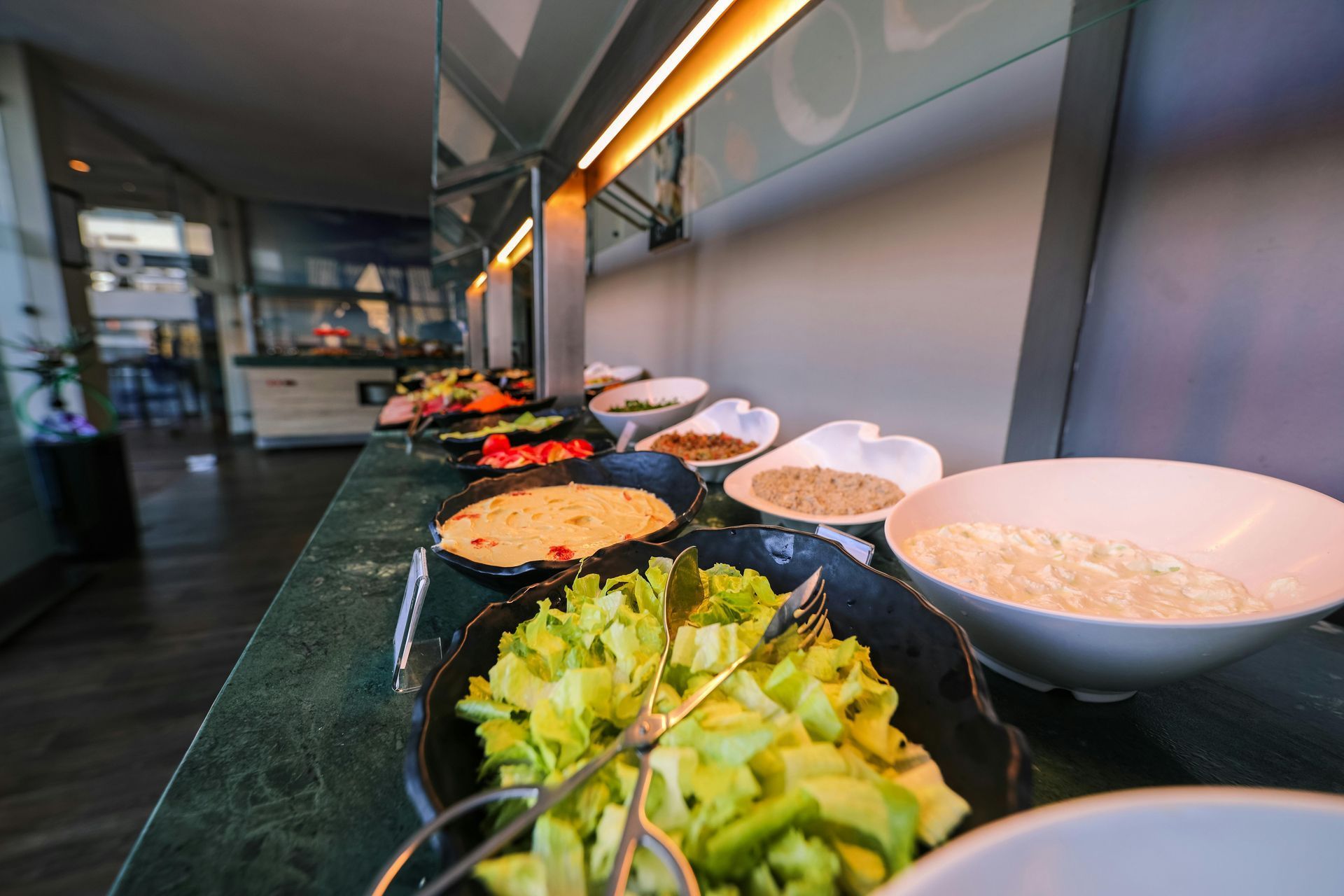 Buffet spread with various salad ingredients, including lettuce and sauces, under bright lights.