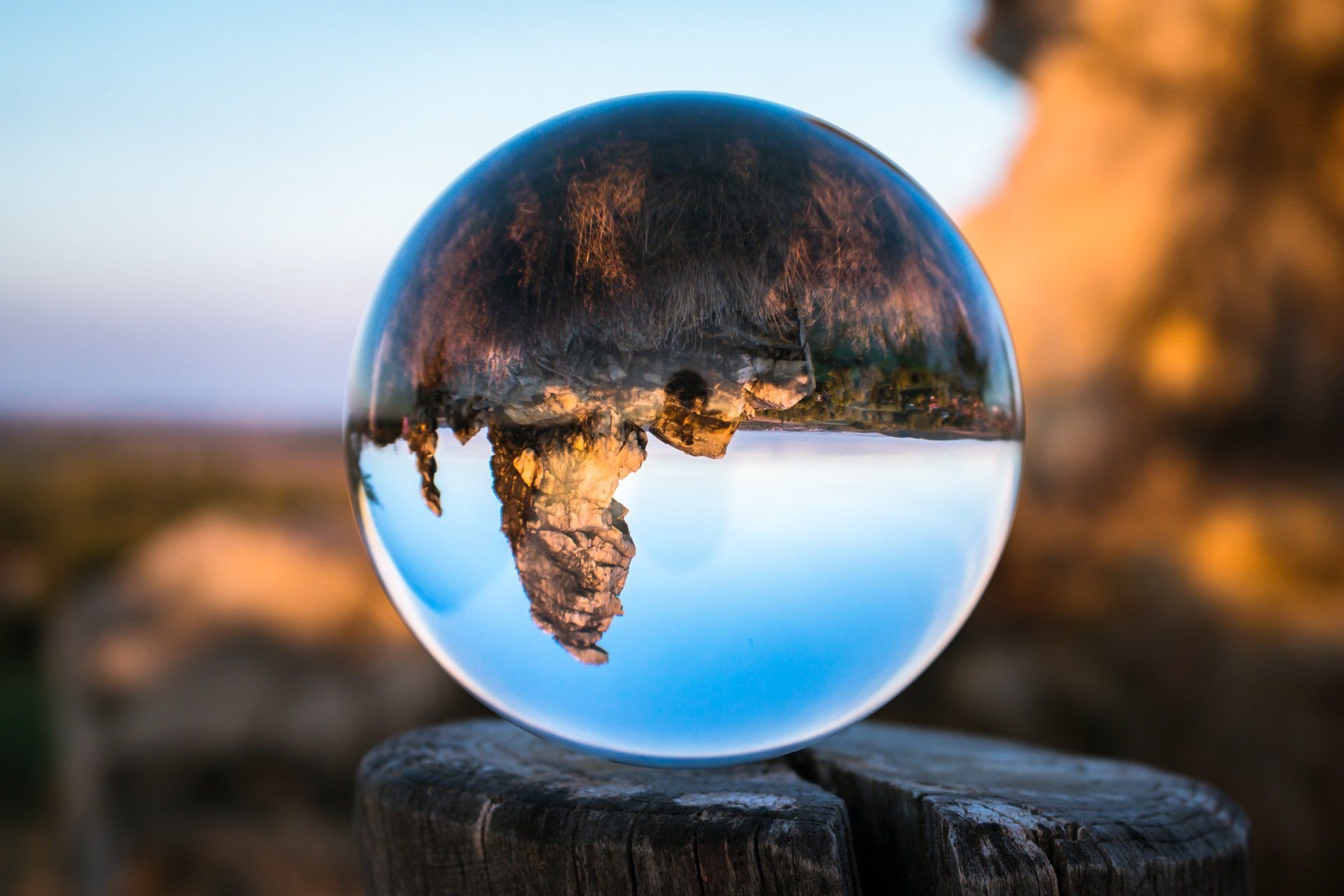 Crystal ball reflecting a landscape with rock formations, blue sky, and a wooden post.