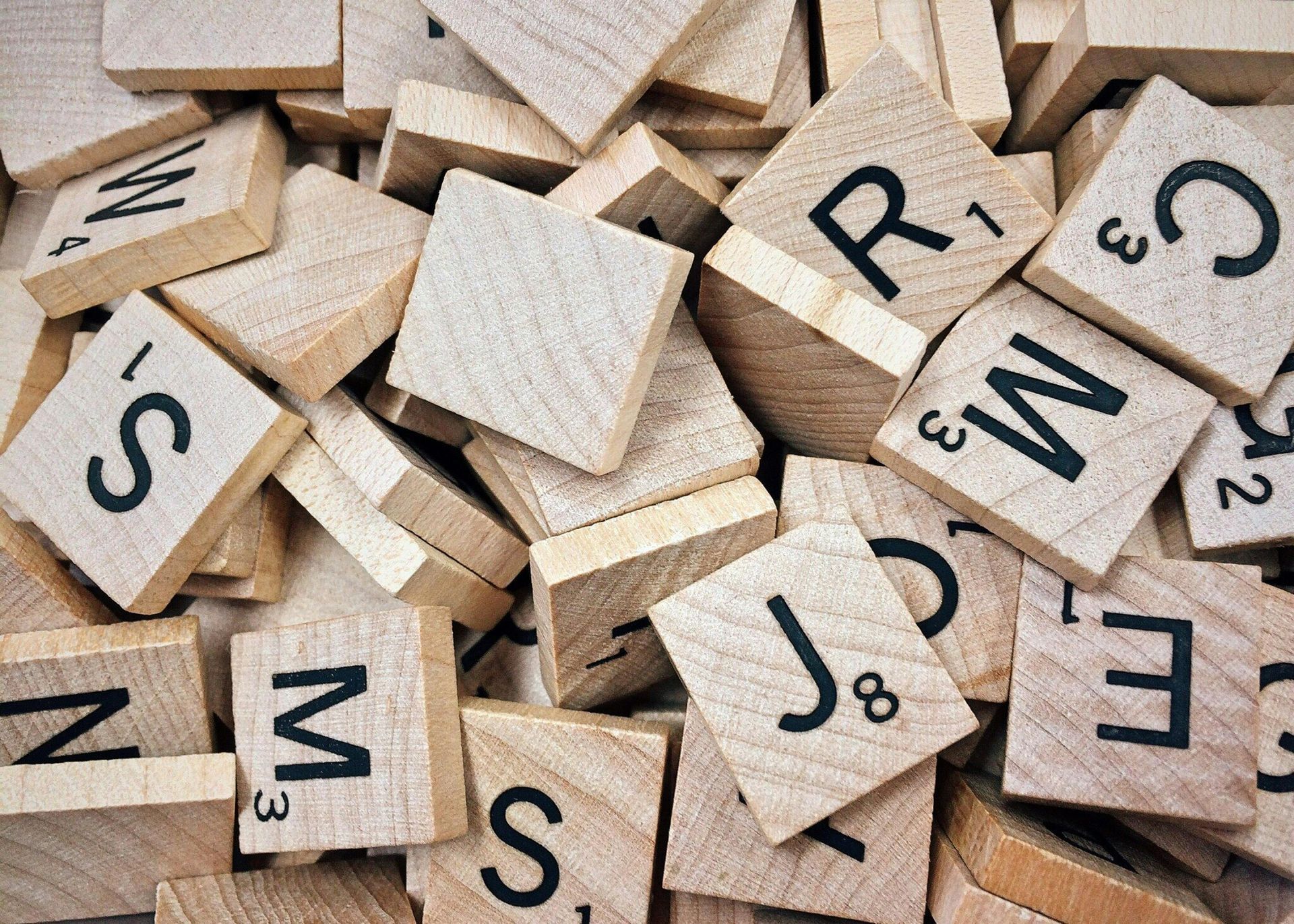Close-up of Scrabble tiles, many mixed together, showing letters and point values on wooden blocks.