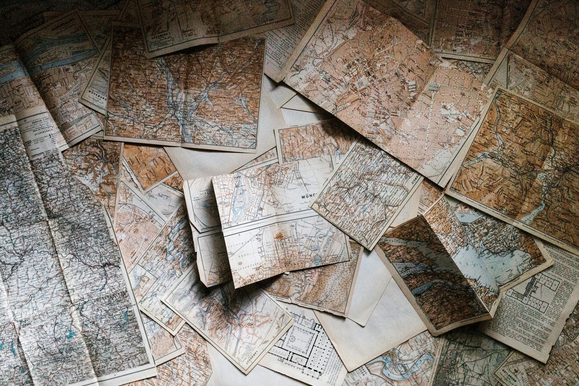 Scattered, aged maps with faded brown and beige tones, overlapping on a surface.