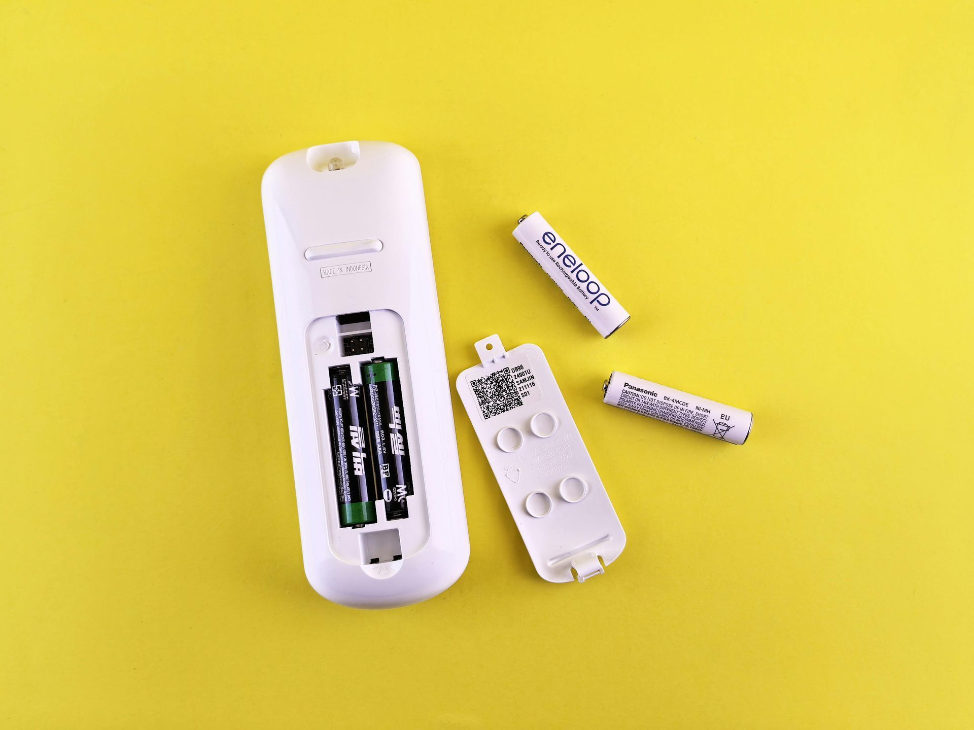 White remote with open battery compartment, three AAA batteries, yellow background.