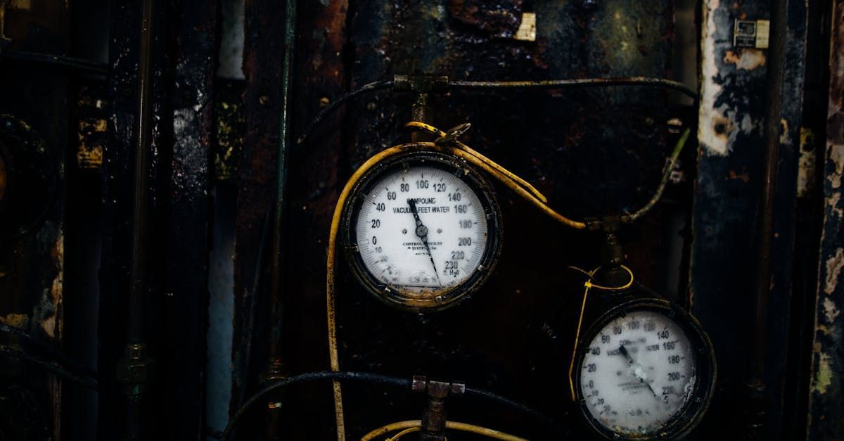 Two old pressure gauges on a dark, weathered metal surface, with a yellow-gold cable.