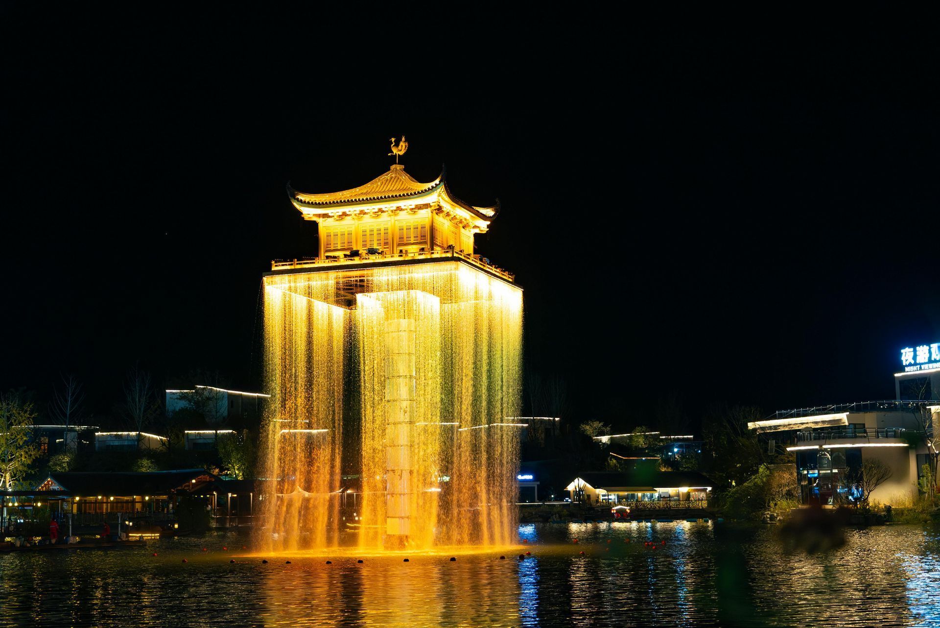 A pagoda-like structure with a glowing waterfall effect, illuminated at night. Reflections in the water.