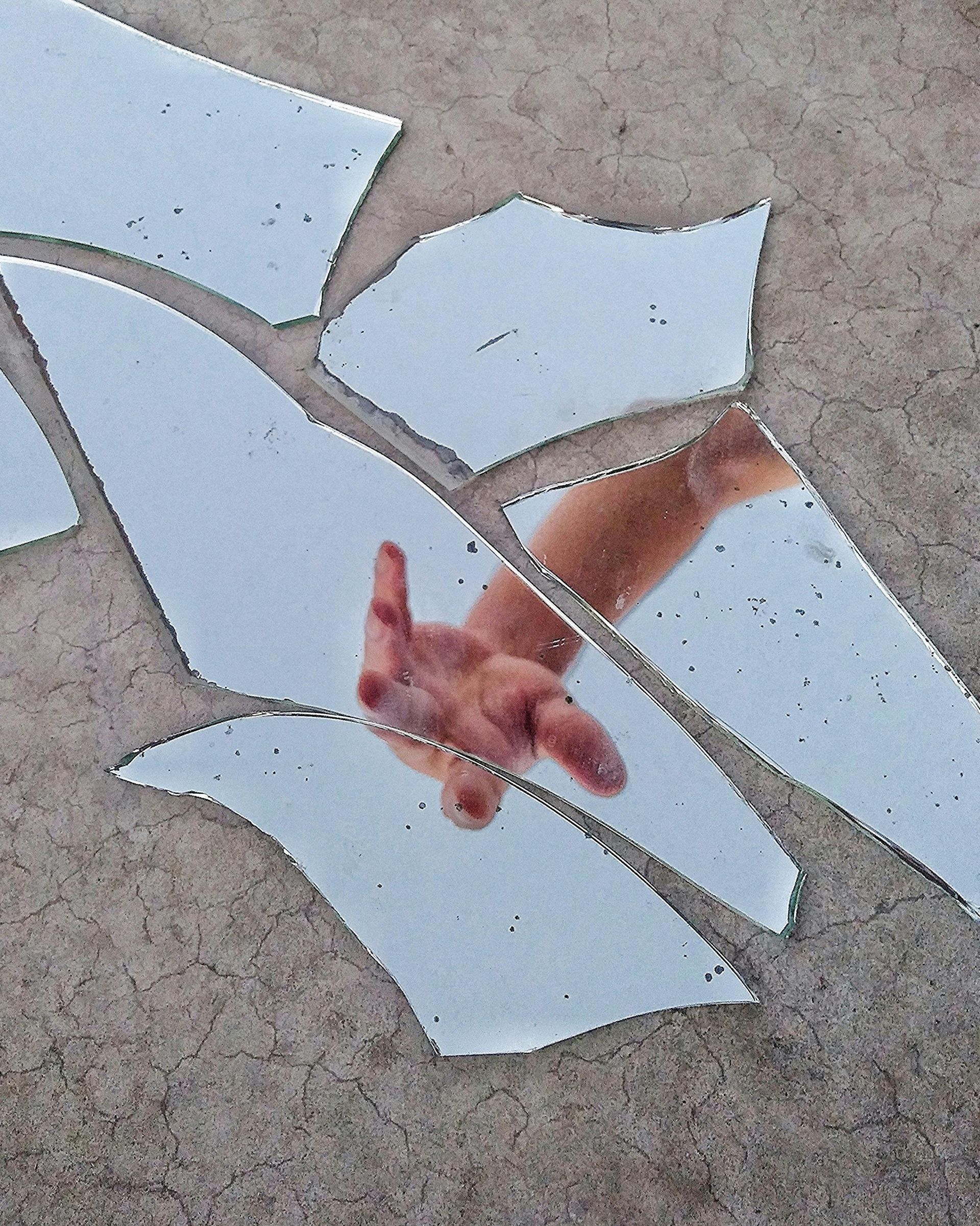 Hand reaching through shards of broken mirror.