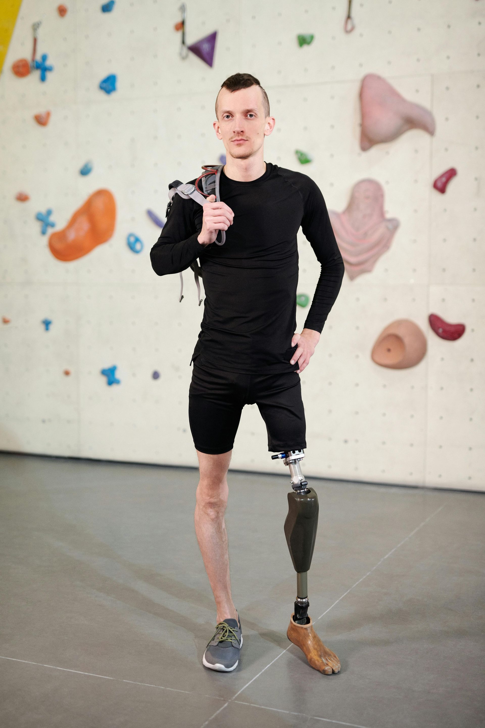 Man with prosthetic leg stands in front of a climbing wall, holding equipment, smiling.