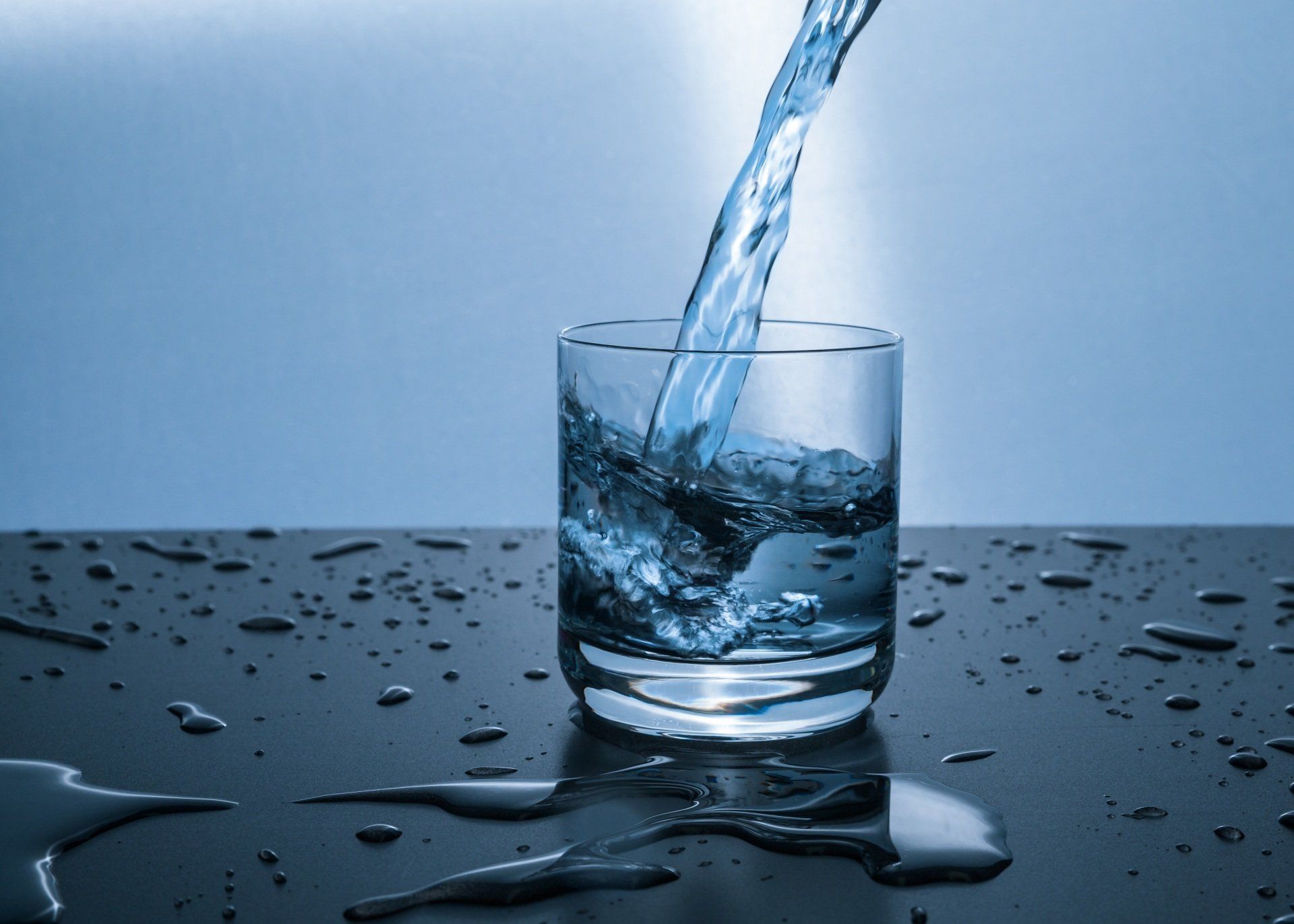 Water pouring into a glass on a wet, dark surface; blue tones.