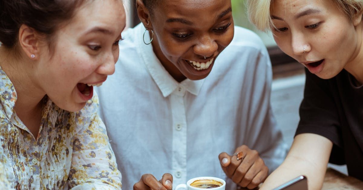 Three people looking at a phone, surprised, one drinking coffee.
