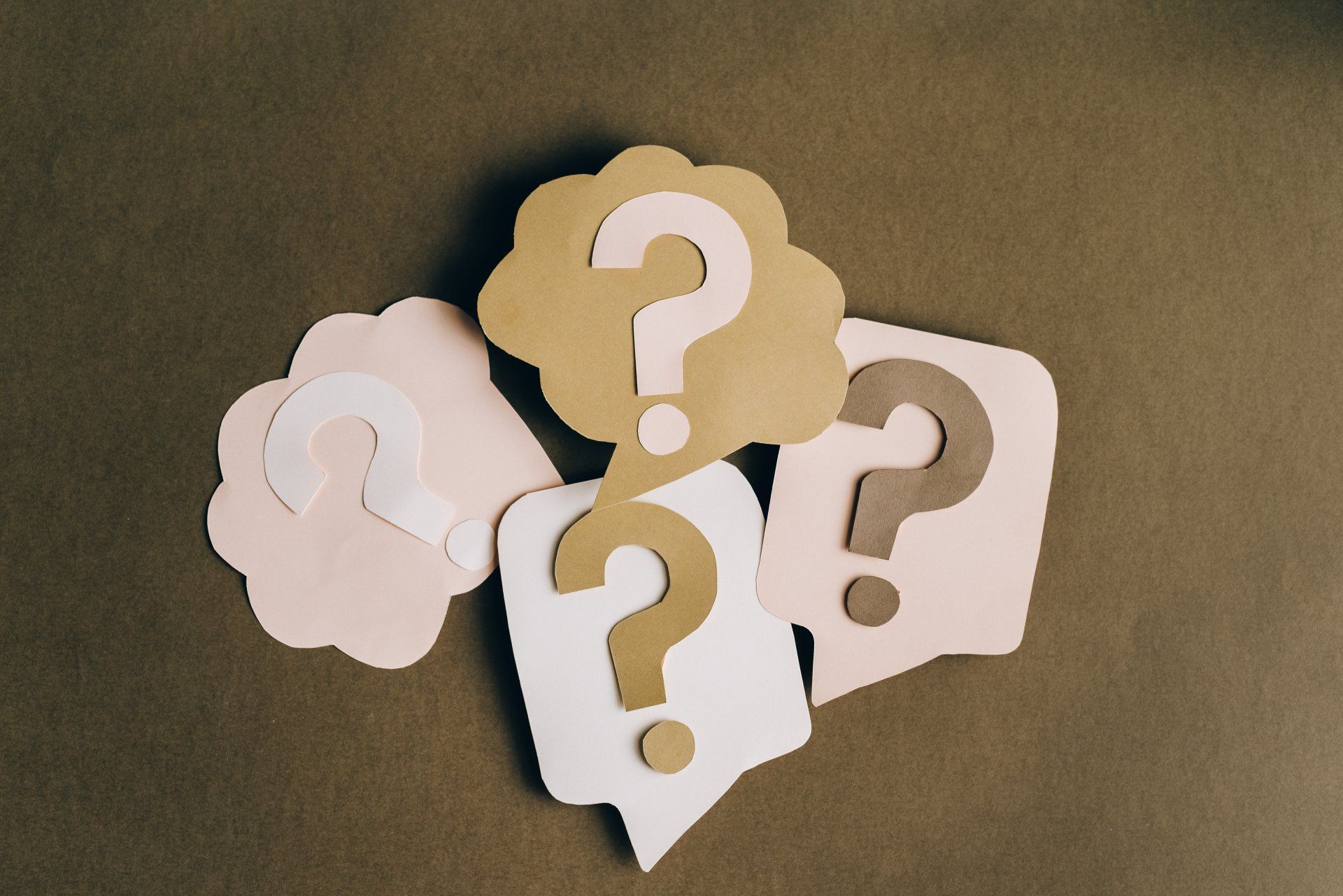 Question marks in various paper speech bubbles, arranged on a brown surface.