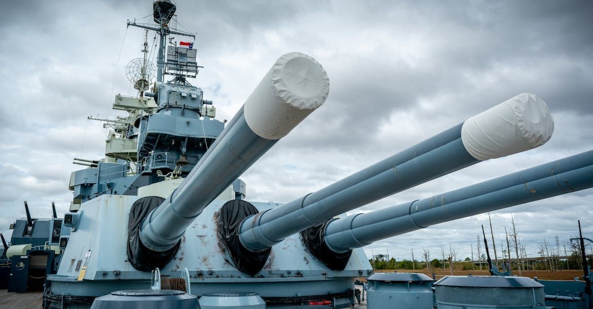 Three large gray battleship cannons with white tips, set against a cloudy sky.