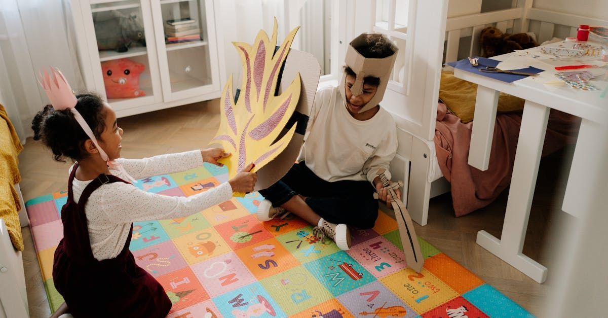 Two children playing with handmade props on a colorful alphabet mat. One holds a flame cutout, the other a sword.