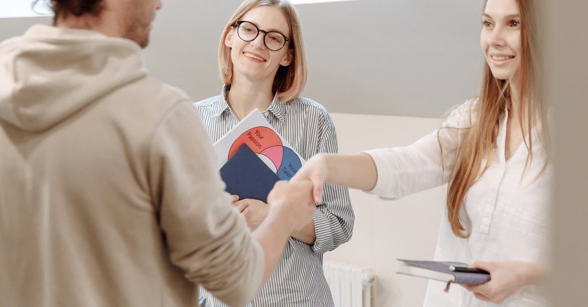 Man shaking hands with a woman; two women in the background. They are in an office, smiling.