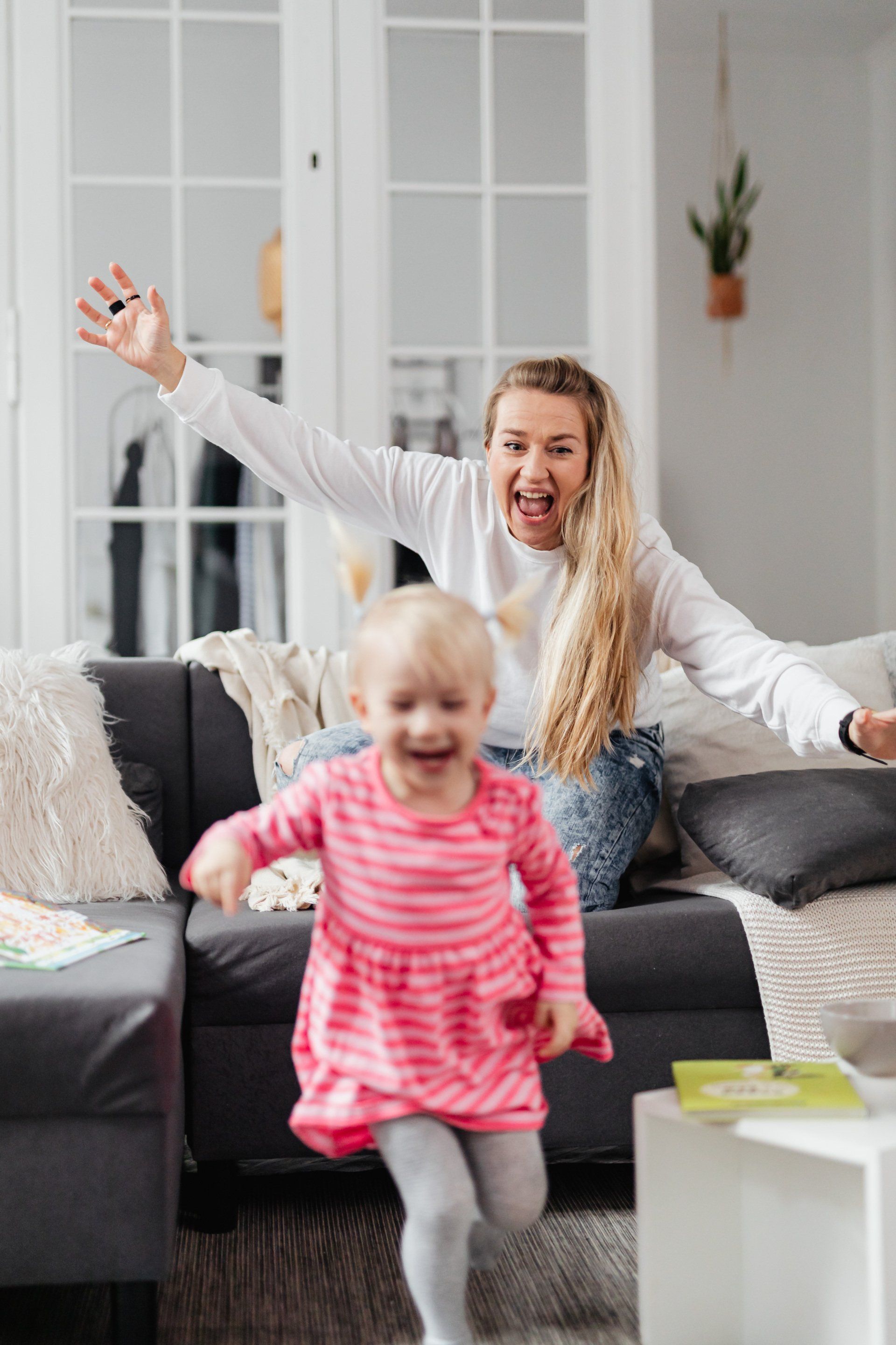 Woman with outstretched arms cheers as toddler runs toward her on a couch.