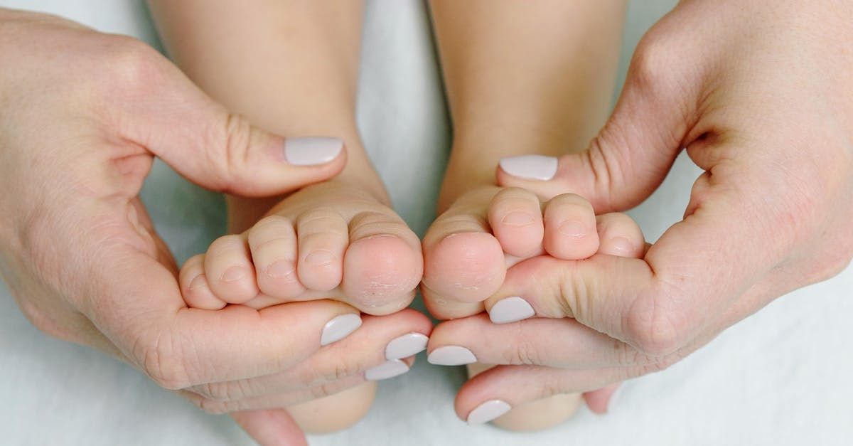 Hands gently holding and massaging a child's bare feet, toes visible, white surface.