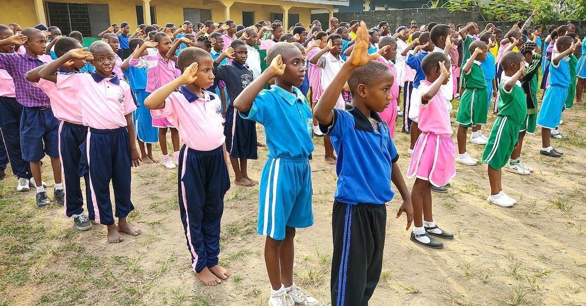 Children in school uniforms saluting outdoors on a grassy field.