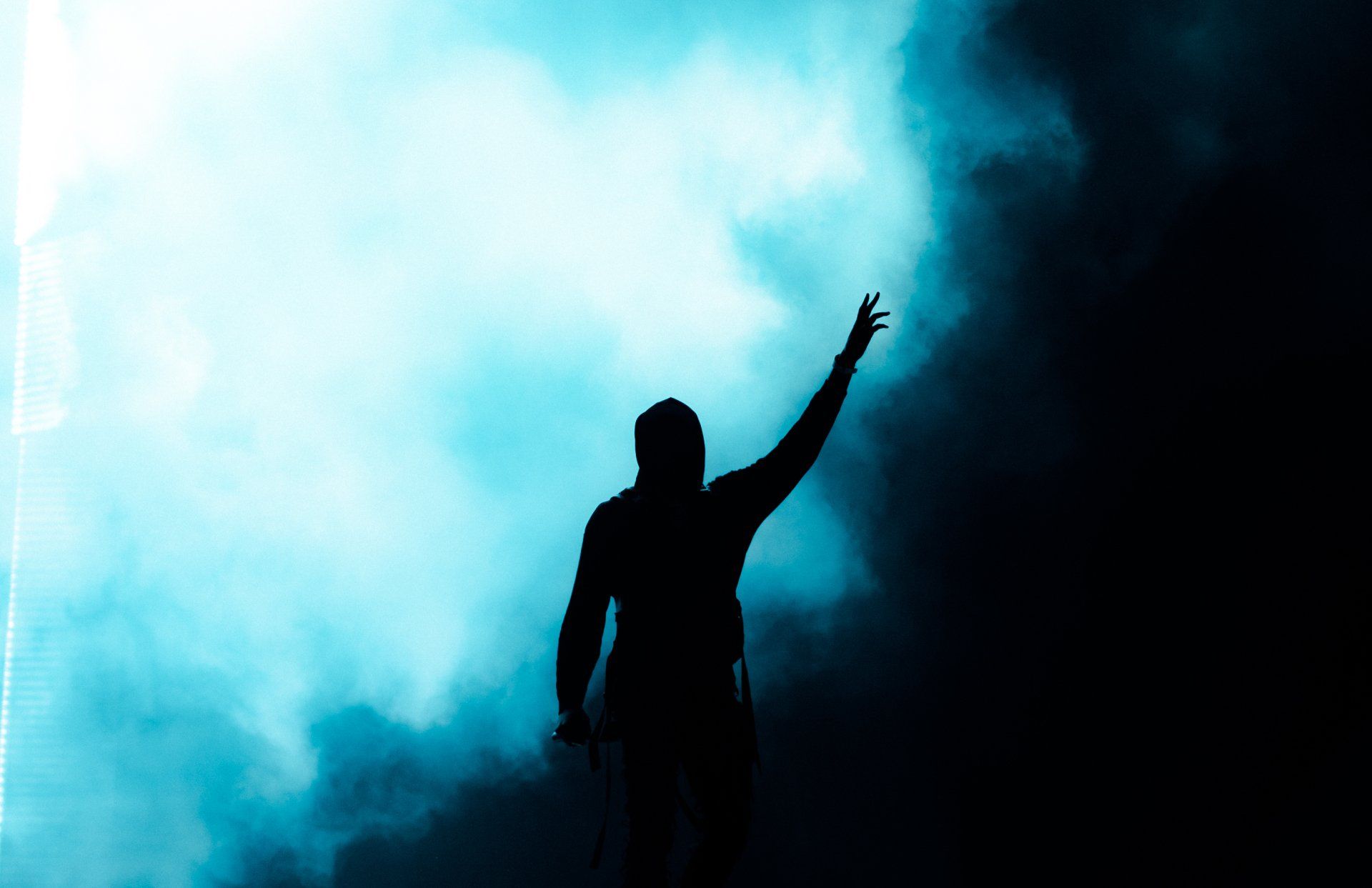 Silhouette of a person with arm raised, against a backdrop of blue and white light and smoke.