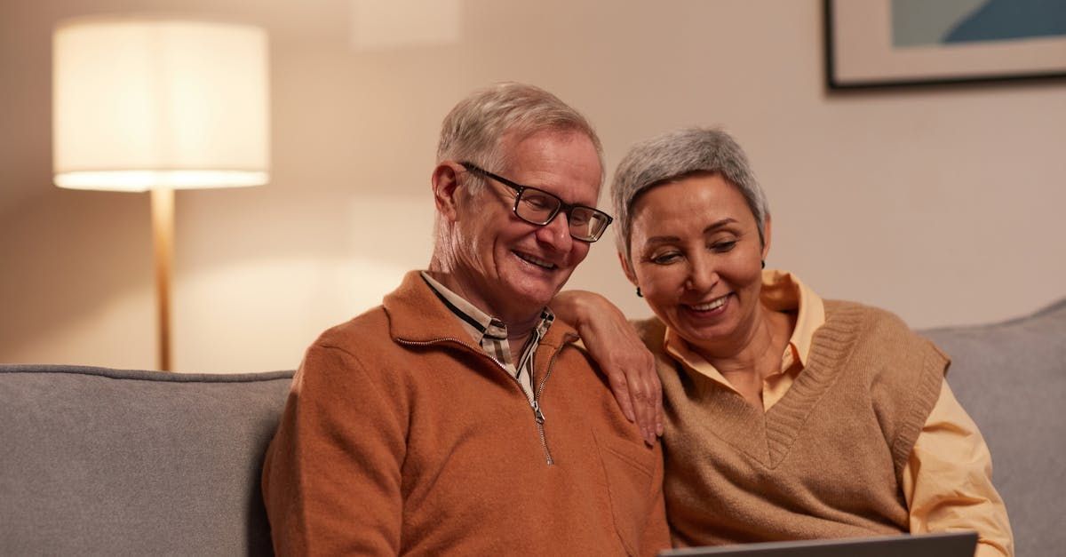 Senior couple smiles while looking at laptop on a sofa in a living room.