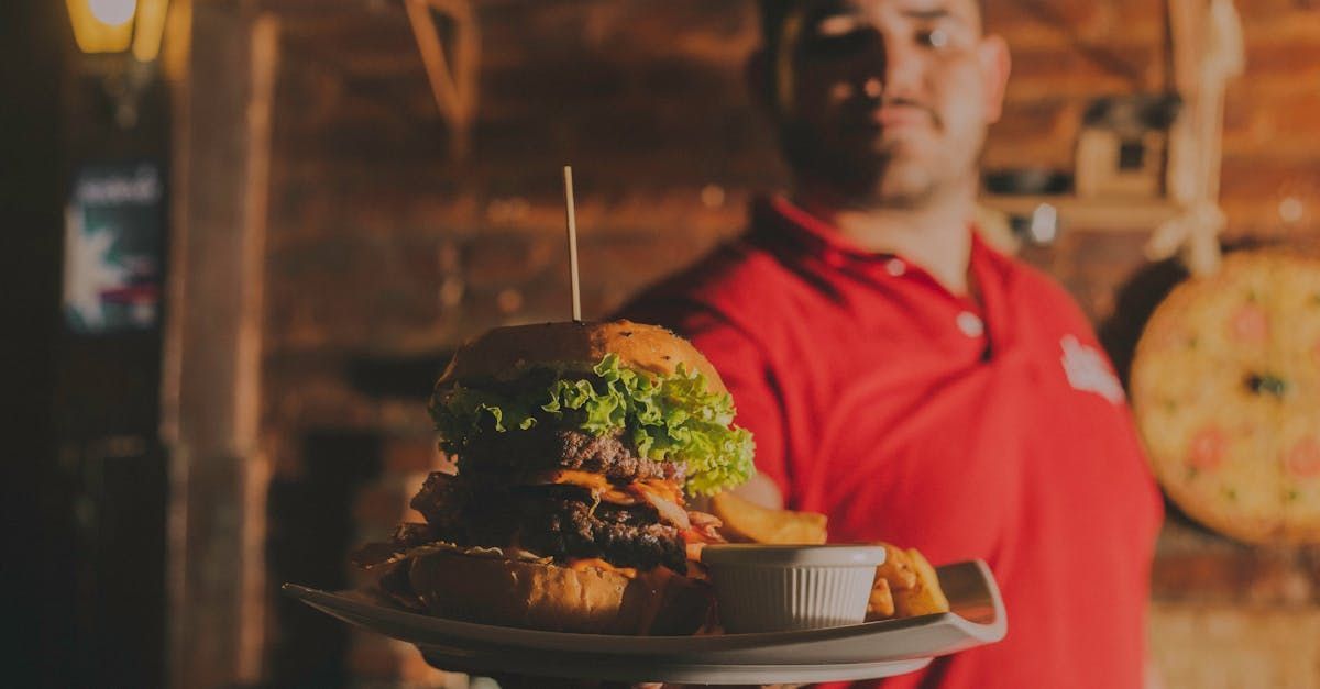 Man in red shirt holding a large burger and fries on a plate.