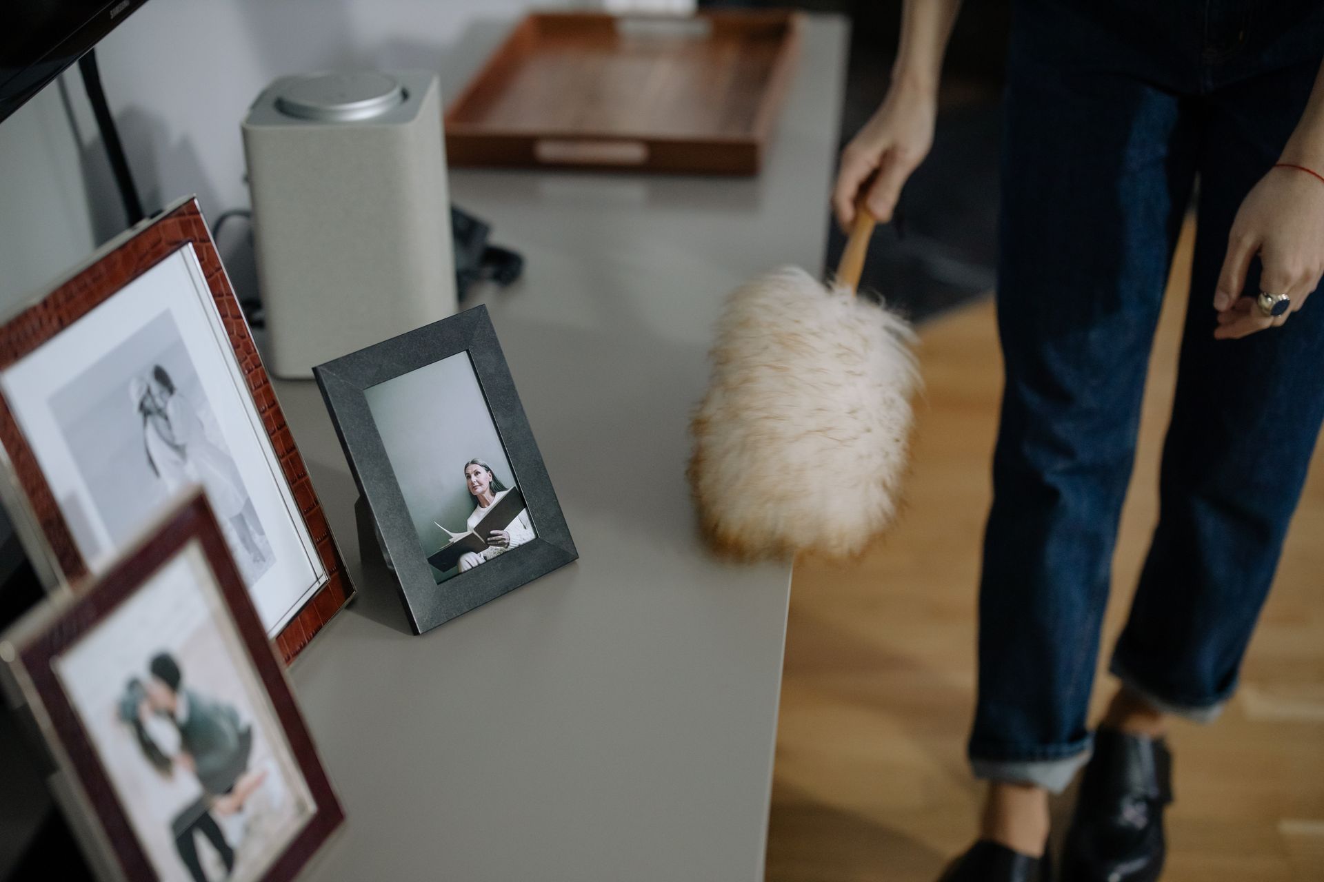 Person dusting framed photos on a gray surface with a fluffy duster.