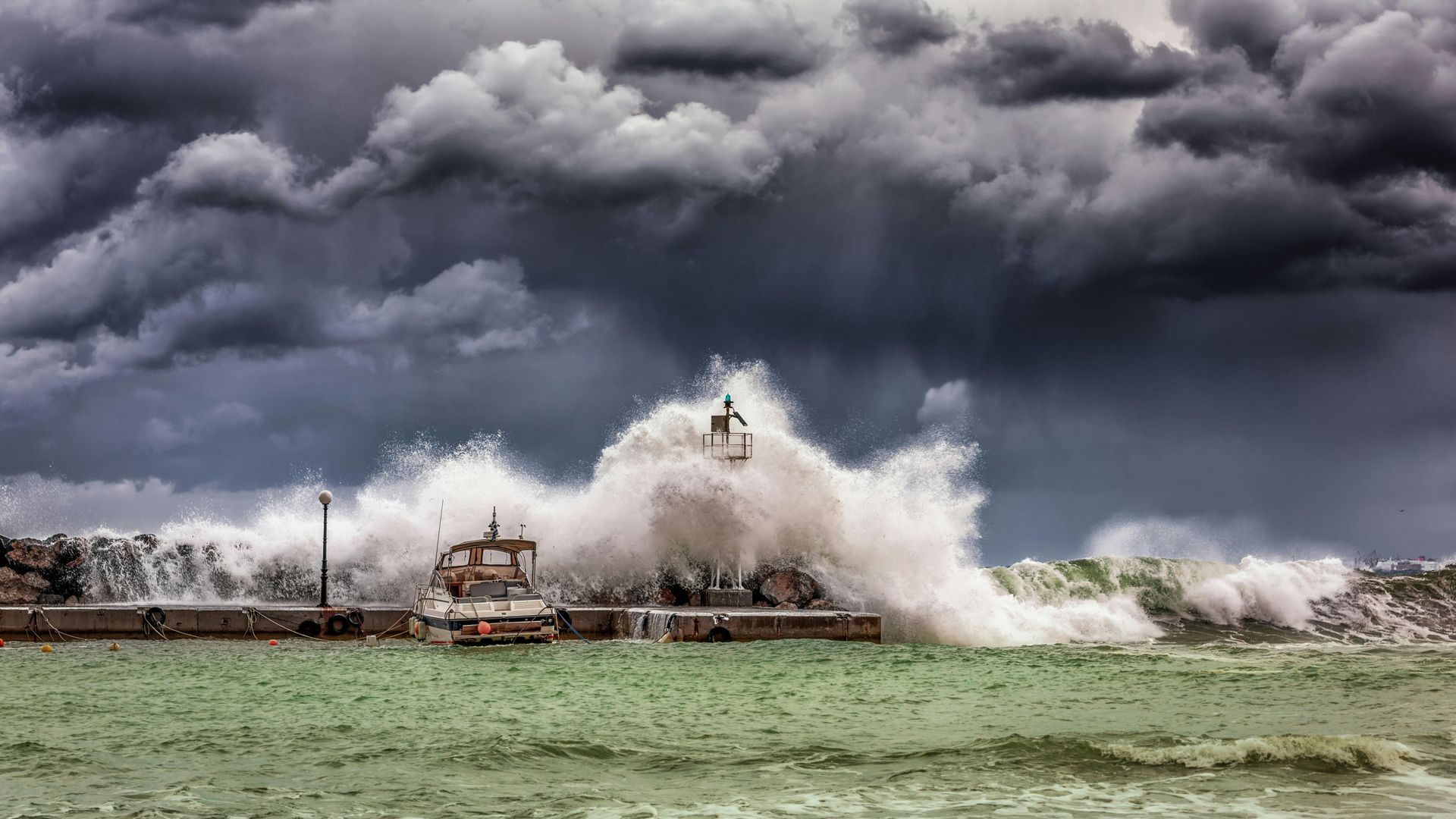 Waves crash over a pier during a storm, boat, person, dark sky.