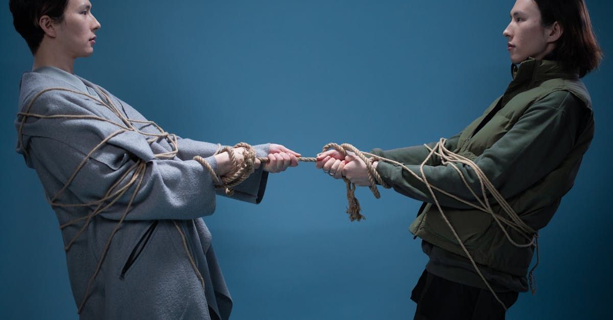 Two people wrapped in rope, pulling on the same rope, blue background.