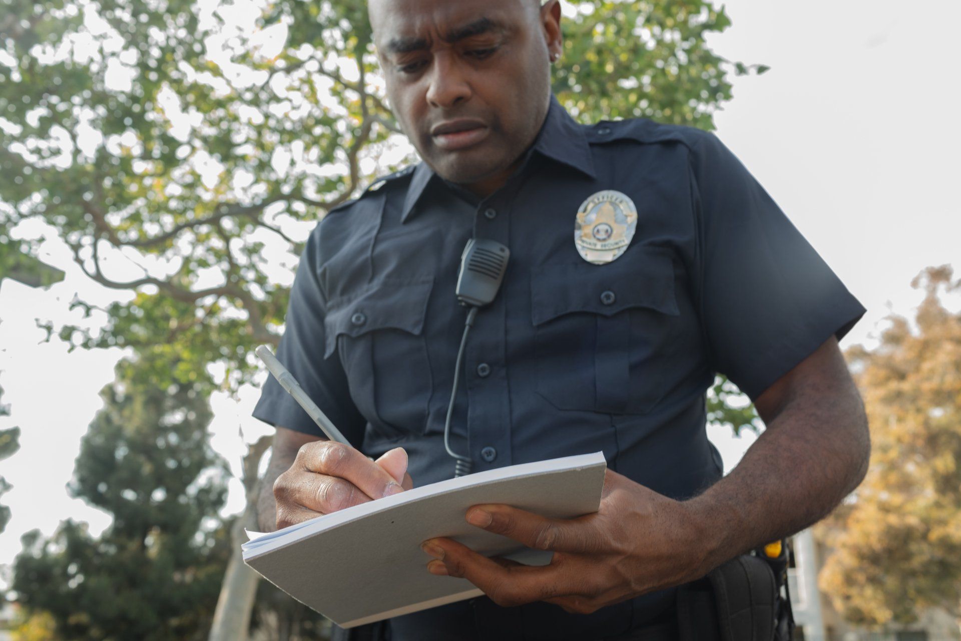 Police officer in uniform writing in a notepad outdoors, focused expression.