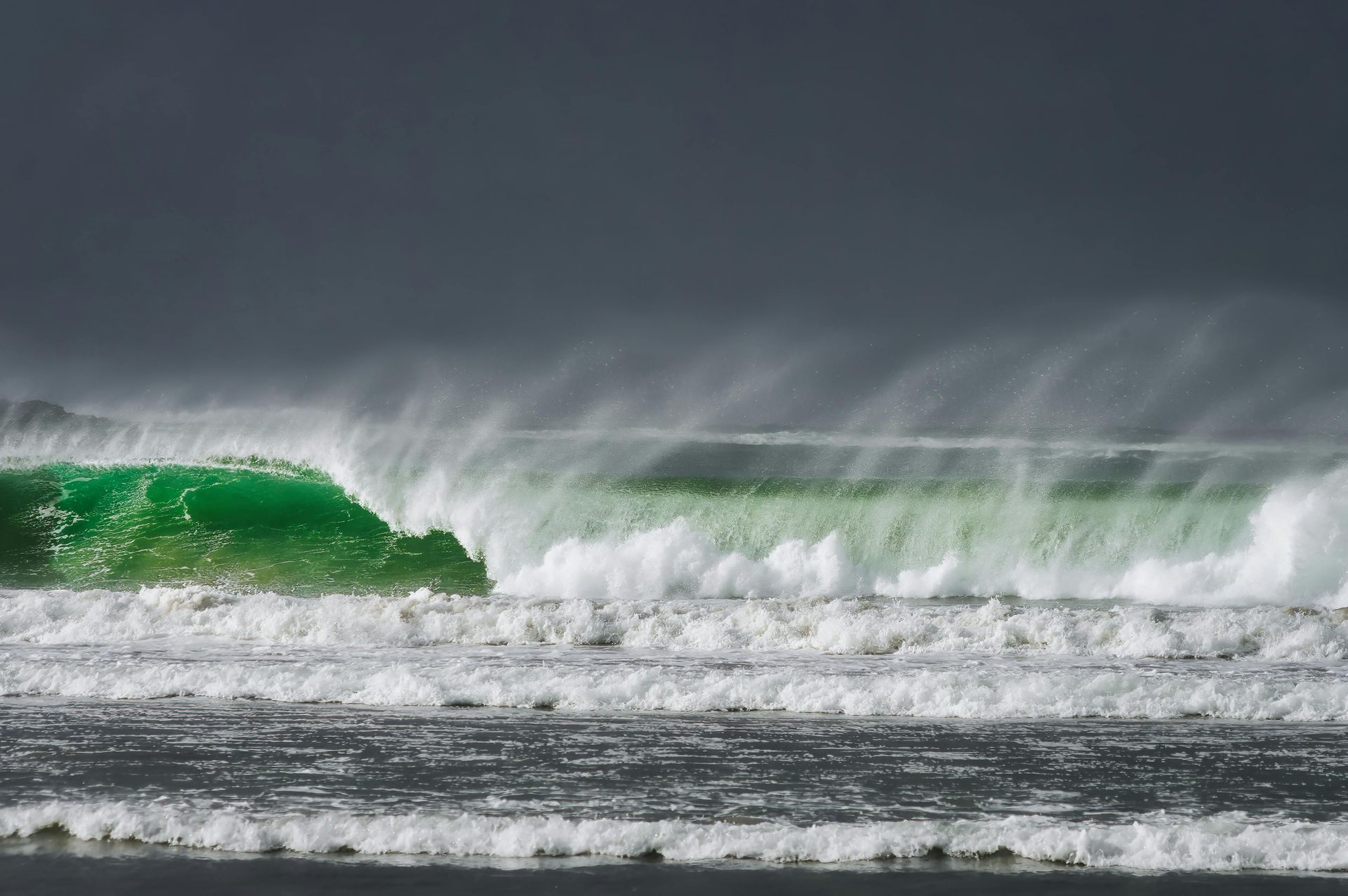 Green wave cresting, white foam, under a dark, stormy sky.