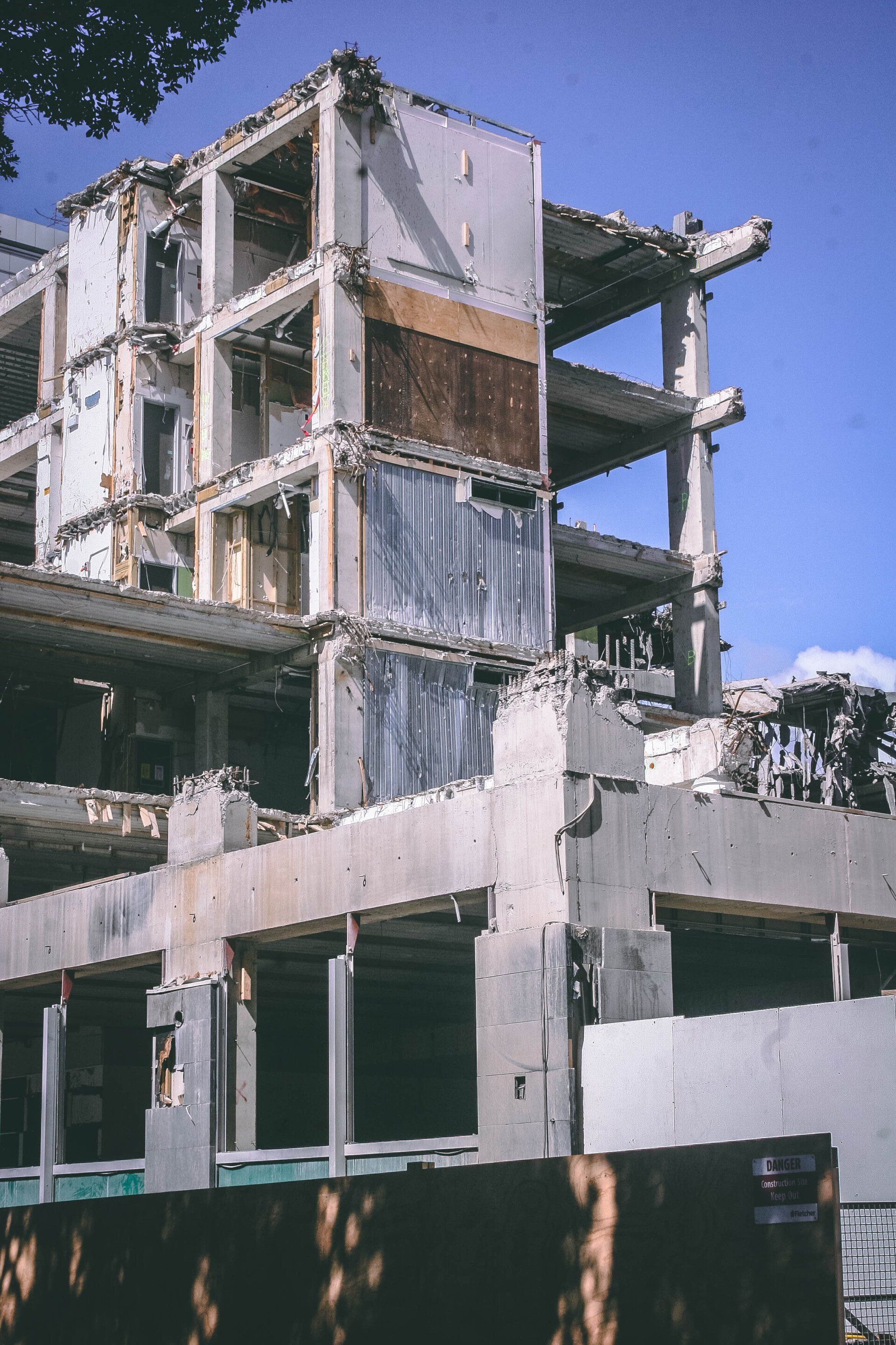 Deconstructed multi-story concrete building with exposed interior framing against a blue sky.