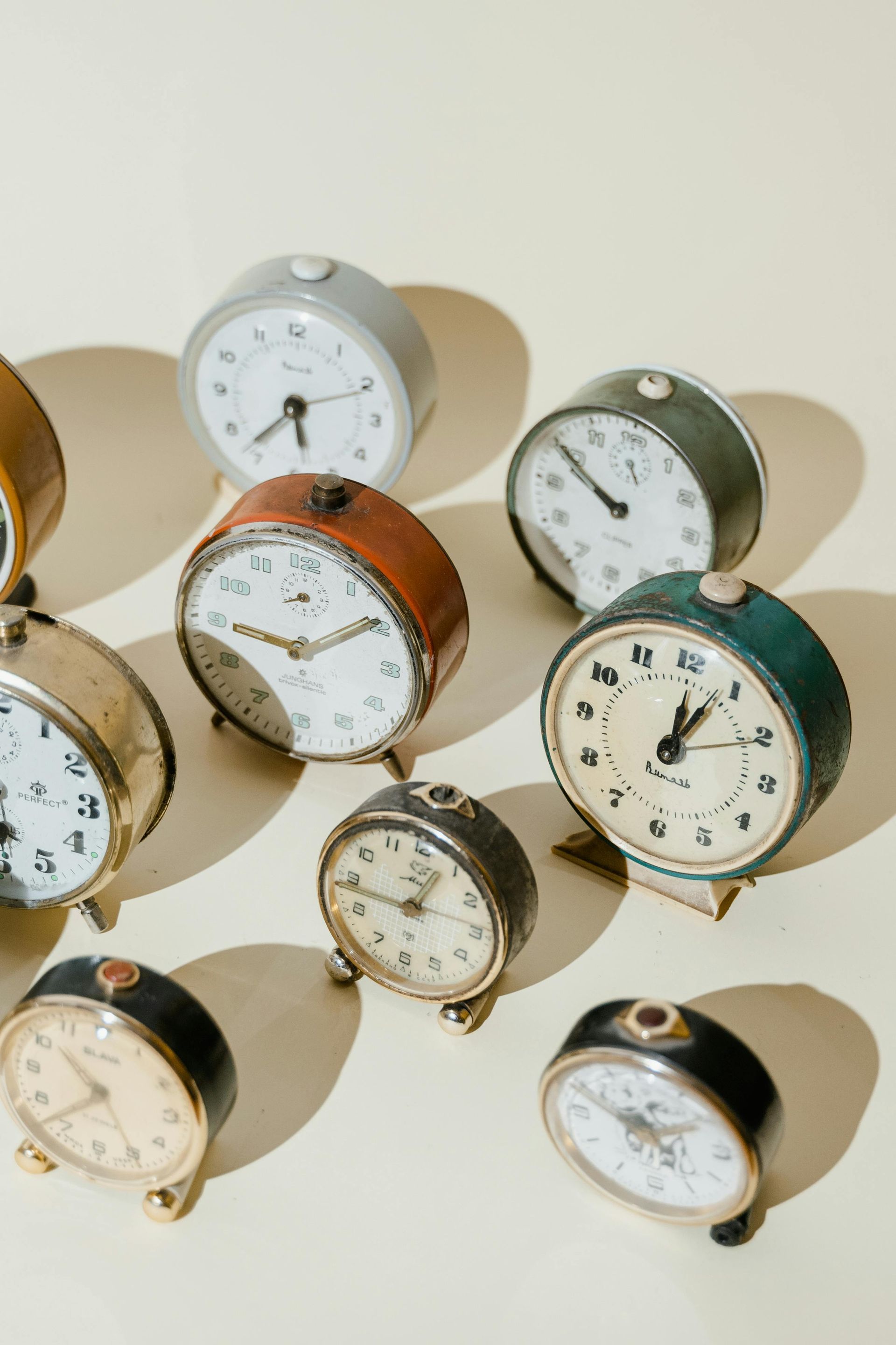 Nine vintage alarm clocks in various colors on a cream background.