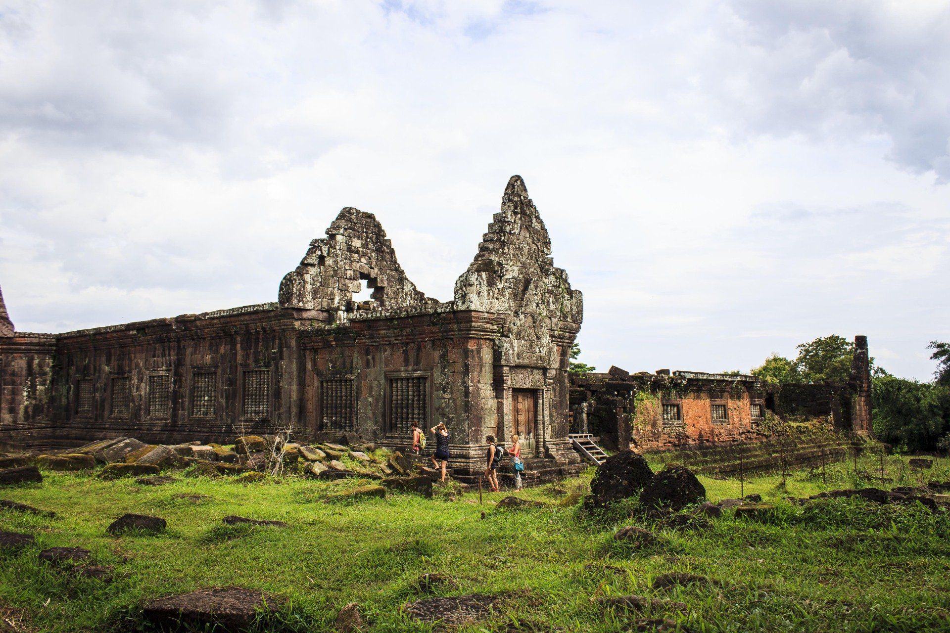 Ancient stone temple ruins in a grassy field under a cloudy sky.
