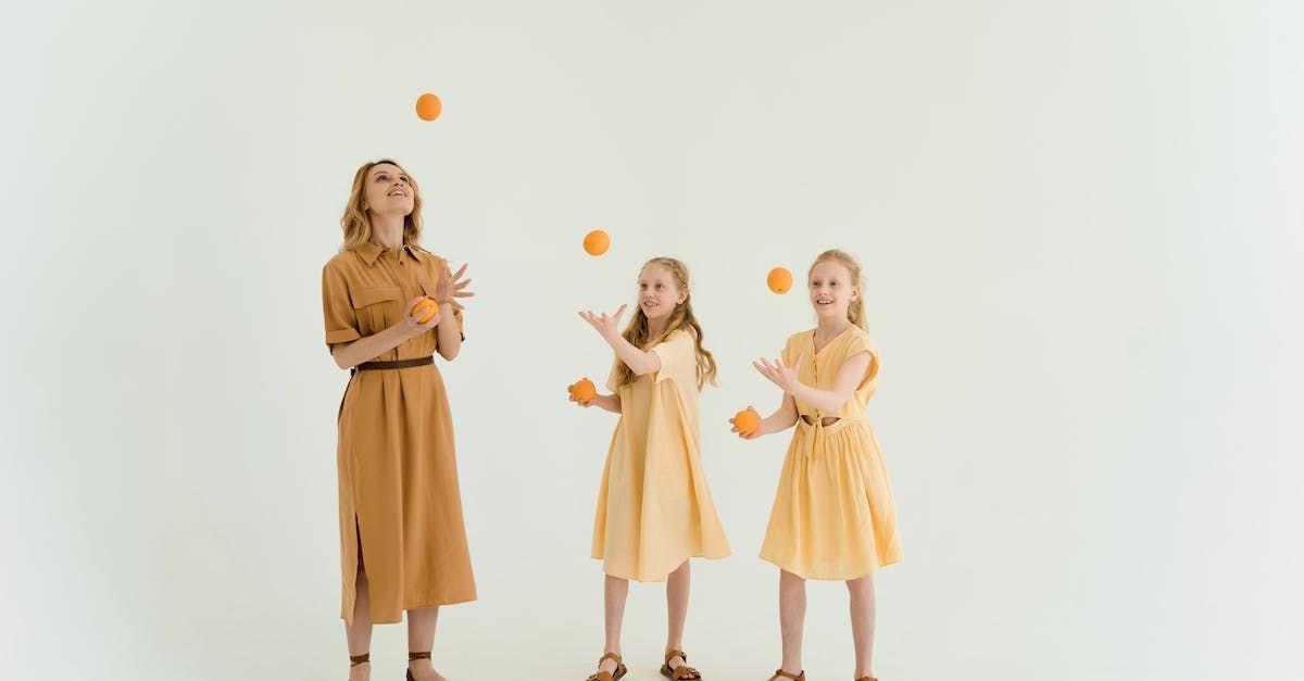 Woman and two girls juggling oranges against a white backdrop.