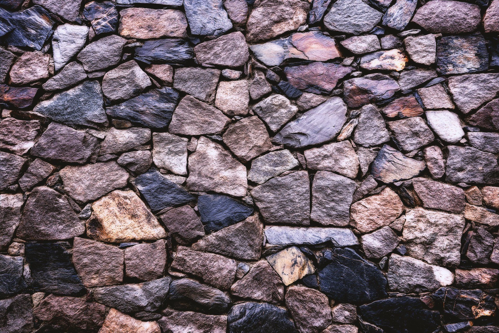 Stone wall made of various shades of brown and gray rocks, tightly fitted together.